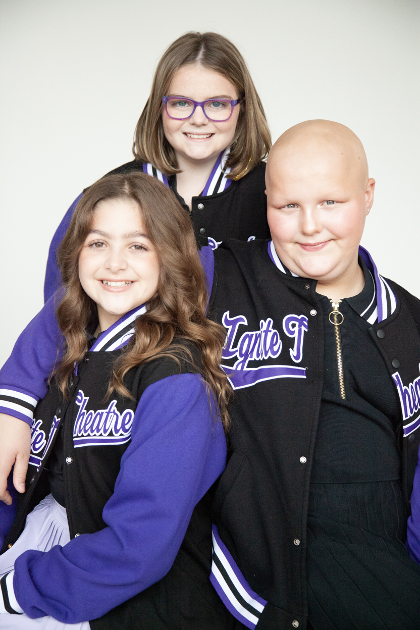 3 young performers wearing Ignite shirts and smiling with a city skyline behind them.